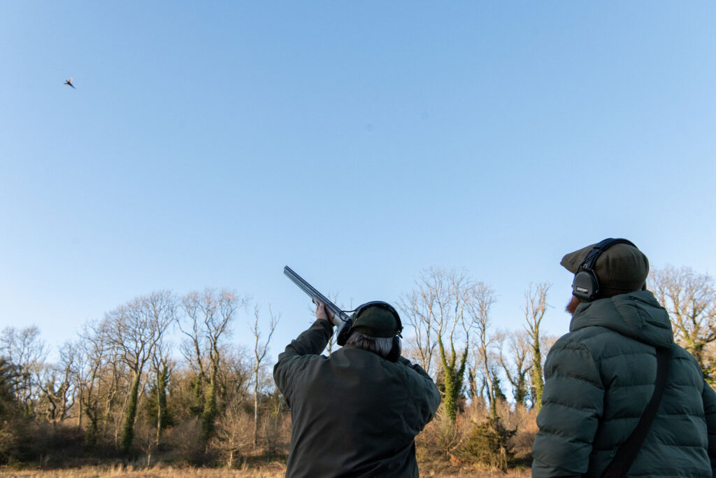 Gun with loader taking aim at a pheasant on a sunny day at Badminton Estate